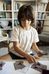 Portrait of boy sitting at table with playing cards at home - VABF02620