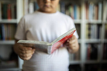 Junge steht vor einem Bücherregal und hält ein Buch, Nahaufnahme - VABF02628