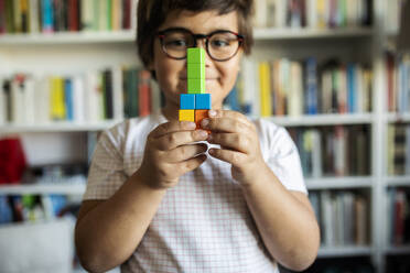 Smiling little boy with glasses playing with building blocks at home - VABF02636