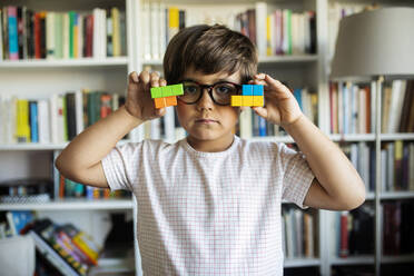 Porträt eines ernsten kleinen Jungen mit Brille, der zu Hause mit Bauklötzen spielt - VABF02637