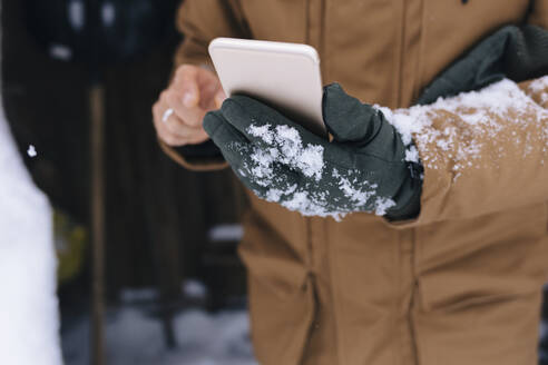 Man's hand holding smartphone in winter, close-up - KNTF04407