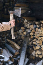 Männerhand, die eine Axt vor einem Stapel Brennholz im Winter hält - KNTF04420