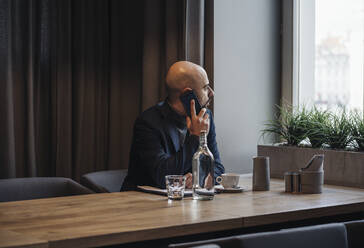 Geschäftsmann mit Smartphone in einem Café, der aus dem Fenster schaut - AHSF01869