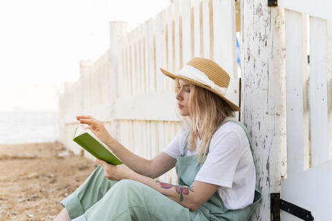 Junge Frau verbringt einen Tag am Meer und liest ein Buch am Strand, lizenzfreies Stockfoto