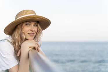 Young woman spending a day at the seaside, leaning on railing, portrait - AFVF05408