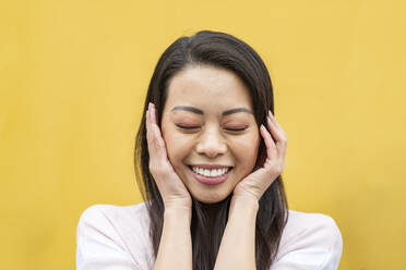 Porträt einer glücklichen Frau mit geschlossenen Augen vor gelbem Hintergrund - WPEF02613