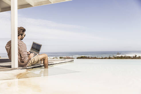 Man working on laptop next to pool at a beach house - SDAHF00159
