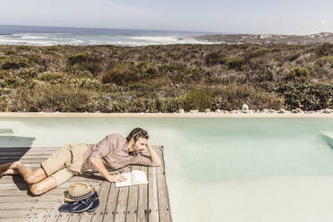 Man lying next to a pool with a notebook - SDAHF00162