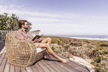 Mann liest ein Buch auf einer Terrasse an der Küste - SDAHF00164