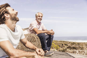 Vater und erwachsener Sohn, die auf einer Terrasse am Meer zusammen abhängen und Spaß haben - SDAHF00167
