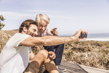 Vater und erwachsener Sohn machen ein Selfie und haben Spaß zusammen auf einer Terrasse am Meer - SDAHF00168