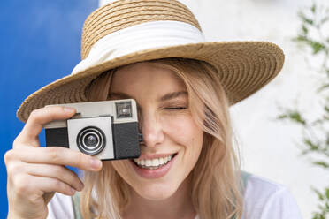 Porträt einer lächelnden jungen Frau mit Strohhut, die ein Foto mit der Kamera macht - AFVF05439