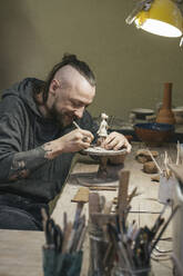 Potter working on a tiny figurine in workshop - VPIF02005