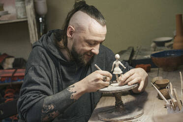 Potter working on a tiny figurine in workshop - VPIF02006