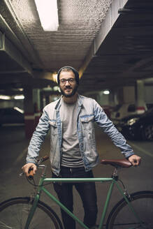 Junger Mann steht mit seinem Fixie-Fahrrad im Parkhaus - RAEF02331