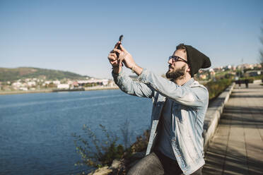 Junger Mann macht Smartphone-Selfies am Meer - RAEF02338