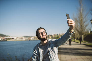 Junger Mann macht Smartphone-Selfies am Meer - RAEF02339
