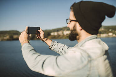 Young man taking smartphone selfies by the sea - RAEF02340