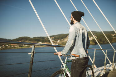 Young man commuting in the city with fis fixie bike, looking at the sea - RAEF02341