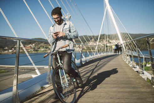 Junger Mann beim Pendeln in der Stadt mit seinem Fixie-Fahrrad, mit Smartphone - RAEF02343