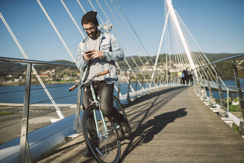 Young man commuting in the city with his fixie bike, using smartphone - RAEF02343