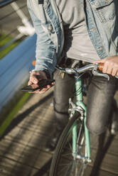 Junger Mann beim Pendeln in der Stadt mit seinem Fixie-Fahrrad, mit Smartphone - RAEF02344