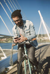 Junger Mann beim Pendeln in der Stadt mit seinem Fixie-Fahrrad, mit Smartphone - RAEF02345