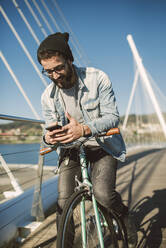 Young man commuting in the city with his fixie bike, using smartphone - RAEF02345