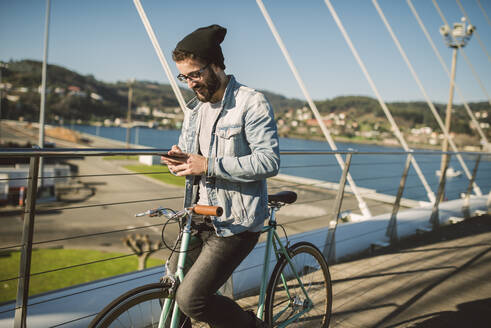 Junger Mann beim Pendeln in der Stadt mit seinem Fixie-Fahrrad, mit Smartphone - RAEF02346