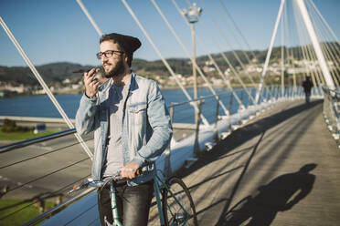 Junger Mann beim Pendeln in der Stadt mit seinem Fixie-Fahrrad, mit Smartphone - RAEF02347