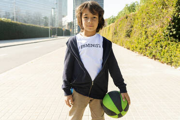 Little boy standing in the street with print on t-shirt, saying Feminist, holding ball - VABF02647
