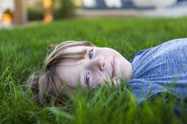 Porträt eines lächelnden sechsjährigen Jungen, der im grünen Gras liegt - MINF13622