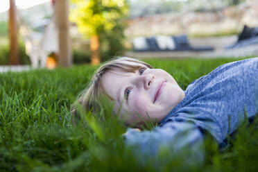 Porträt eines lächelnden sechsjährigen Jungen, der im grünen Gras liegt - MINF13623