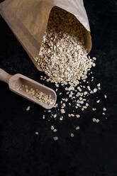 High angle close up of paper bag with oats and wooden spoon on dark background. - MINF13633