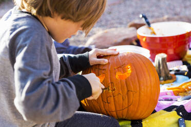 A six year old boy carving pumpkin outdoors at Halloween. - MINF13687