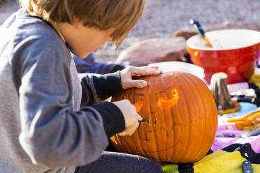 Ein sechsjähriger Junge schnitzt an Halloween im Freien einen Kürbis. - MINF13687