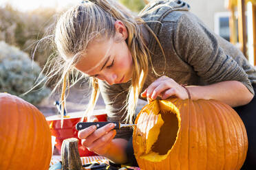 A teenage girl carving a large pumpkin at Halloween. - MINF13688