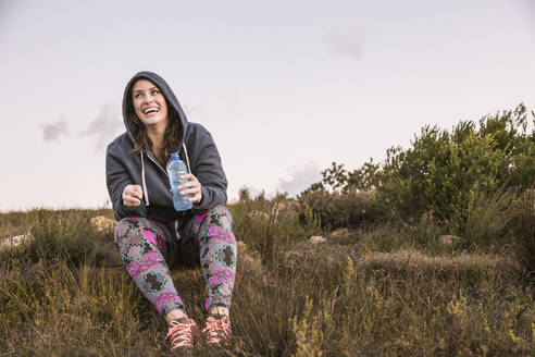 Happy woman with drinking bottle taking a break in the countryside at sunset - SDAHF00210