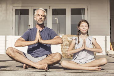 Vater und Tochter sitzen auf der Terrasse im Sonnenschein und machen Yoga - SDAHF00240