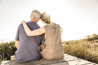 Rear view of couple sitting on boardwalk at sunset looking at view - SDAHF00266