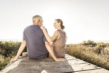 Rear view of couple sitting on boardwalk at sunset - SDAHF00267