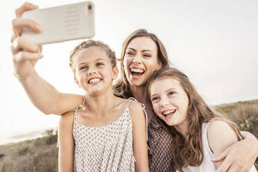 Glückliche Mutter macht ein Selfie mit ihren beiden Töchtern bei Sonnenuntergang - SDAHF00278