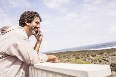 Mann im Bademantel und mit Smartphone telefonierend auf einer Terrasse - SDAHF00288