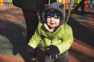 Porträt eines glücklichen kleinen Jungen auf dem Spielplatz an einem sonnigen Wintertag - BZF00531