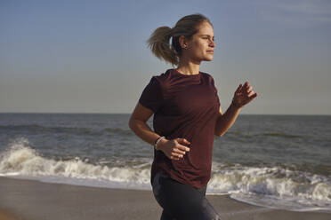 Junge Frau läuft am Strand - PACF00191