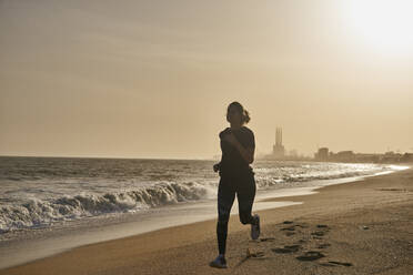 Junge Frau läuft bei Sonnenuntergang am Strand - PACF00192