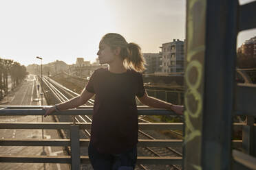 Sportliche junge Frau steht bei Sonnenuntergang auf einer Brücke - PACF00194
