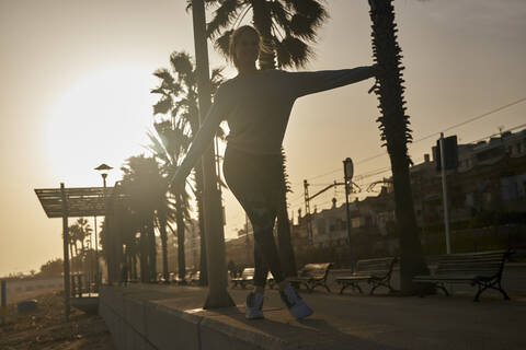 Junge Frau balanciert auf der Promenade am Strand bei Sonnenuntergang, lizenzfreies Stockfoto