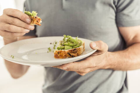 Nahaufnahme eines Mannes, der einen Teller mit einem gesunden Avocadobrot hält, lizenzfreies Stockfoto