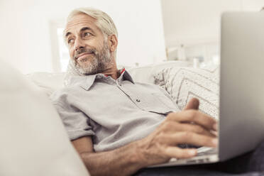 Älterer Mann benutzt Laptop auf der Couch zu Hause - SDAHF00329